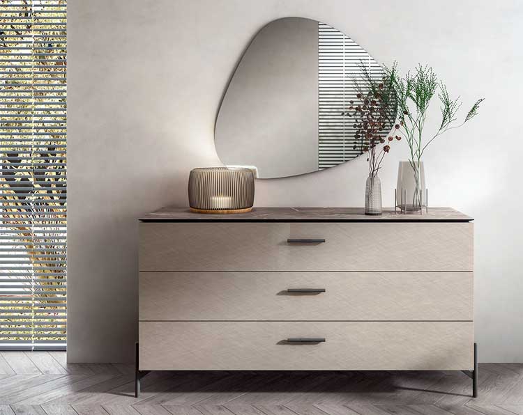 Modern light wood dresser with three drawers, decorative vases, and an irregularly shaped wall mirror above it